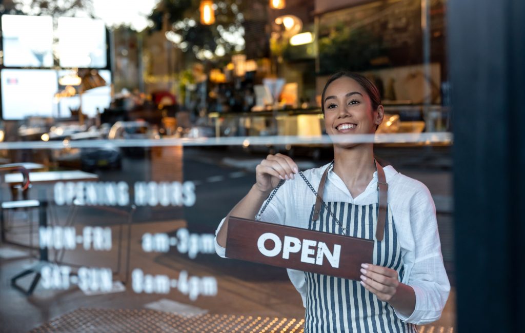 Portrait of a happy woman hanging an open sign at a cafe and smiling - food and drinks concepts